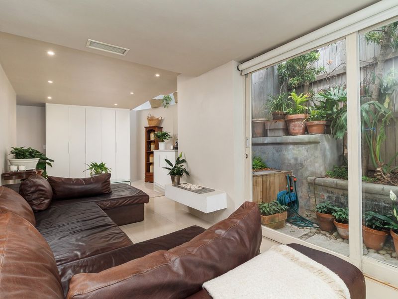 A bright living room featuring tiled floors, recessed lighting, and large sliding glass doors that open onto a private, tiered garden courtyard.