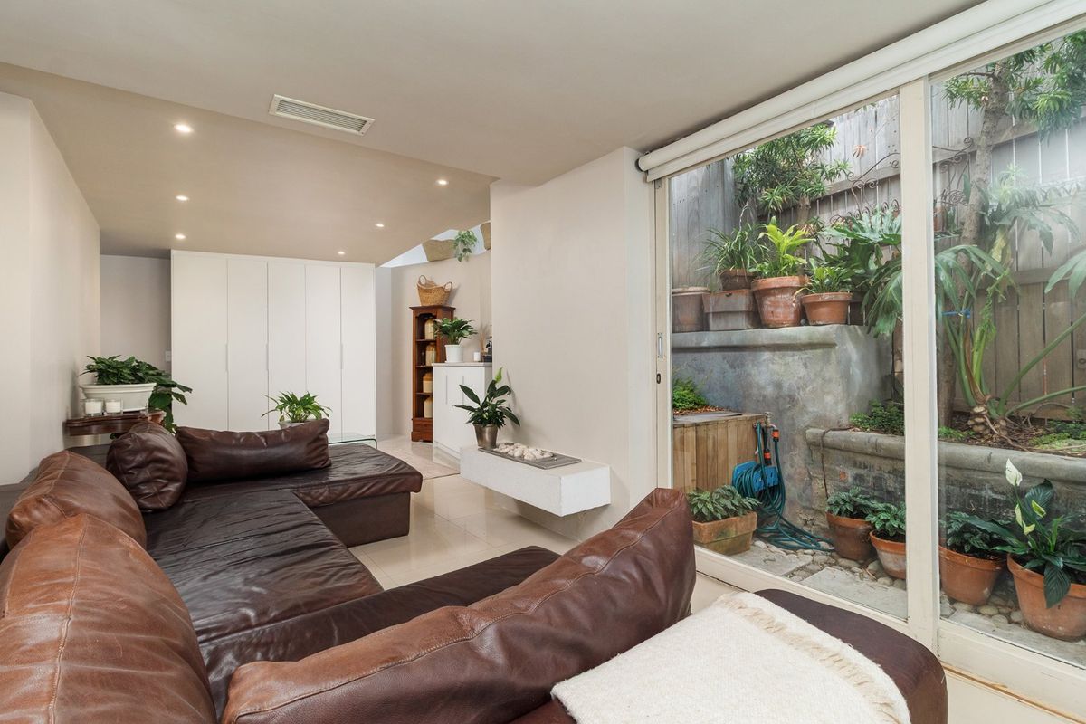 A bright living room featuring tiled floors, recessed lighting, and large sliding glass doors that open onto a private, tiered garden courtyard.
