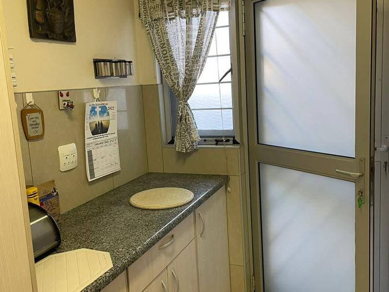 A functional scullery area featuring laminate cabinetry, granite countertops, tiled splashbacks, and a frosted glass door leading to the exterior.