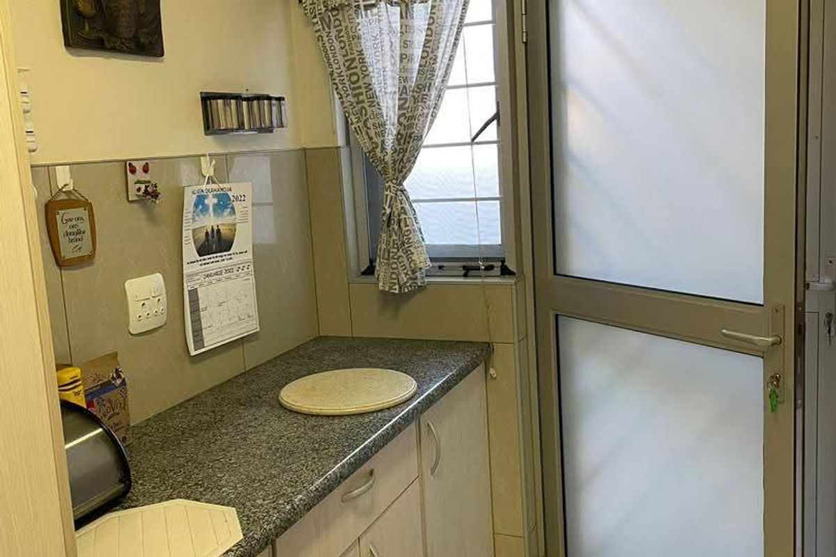A functional scullery area featuring laminate cabinetry, granite countertops, tiled splashbacks, and a frosted glass door leading to the exterior.