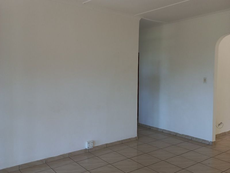 An empty living area featuring neutral tiled flooring and an arched entryway, providing a blank canvas for interior design.