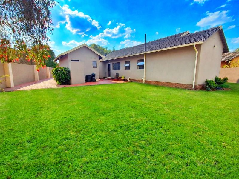 A view of the rear exterior of the house featuring a spacious lawn, paved patio area, and perimeter boundary walls.