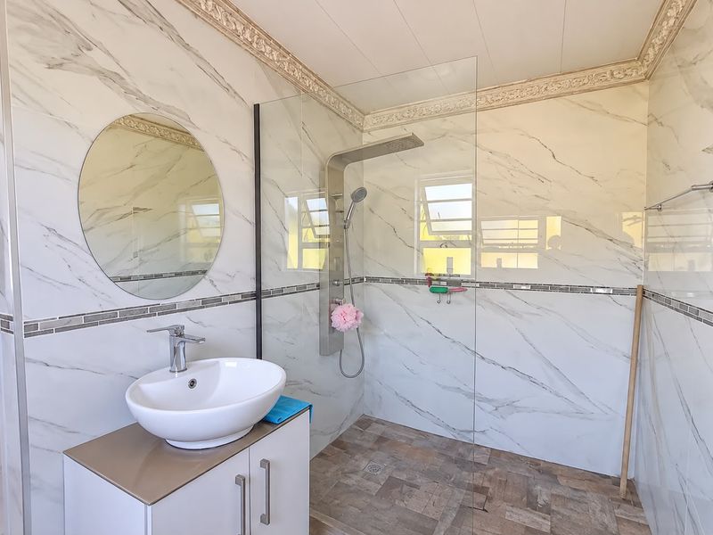 Modern bathroom featuring marble-look wall tiles, a glass shower enclosure with a rainfall shower panel, and a contemporary vessel sink vanity.
