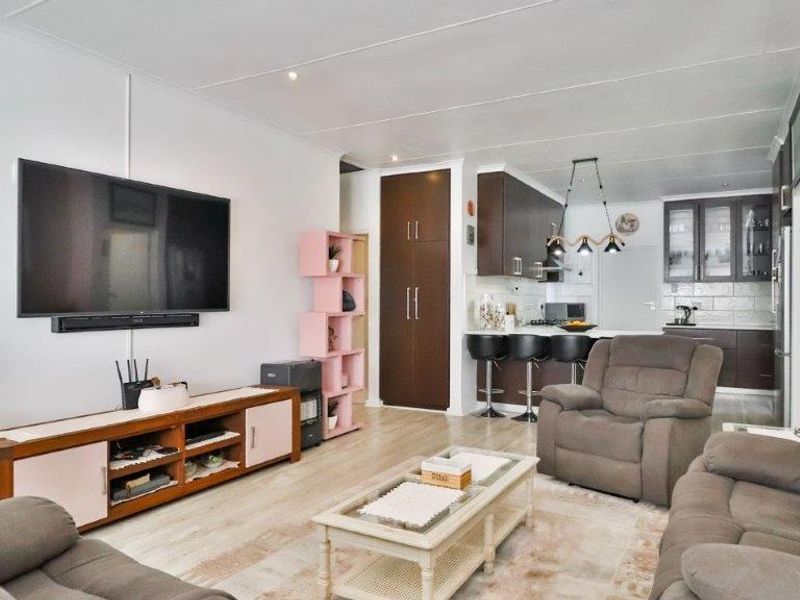 Open-plan living area featuring a modern kitchen with dark cabinetry, a breakfast bar, and light laminate flooring throughout the combined space.