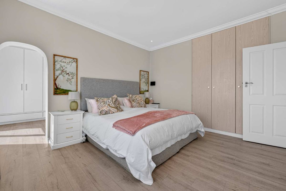 A well-maintained bedroom featuring light wood-look laminate flooring, built-in cupboards, and a classic arched doorway leading to an adjacent space.