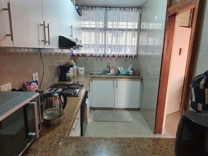 A functional kitchen featuring granite countertops, white cabinetry, an electric hob with extractor fan, and tiled finishes throughout.