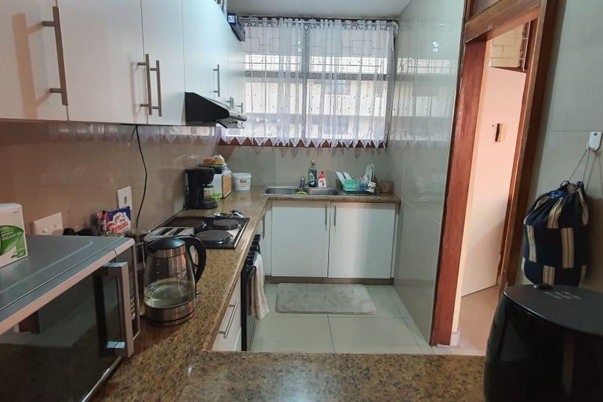 A functional kitchen featuring granite countertops, white cabinetry, an electric hob with extractor fan, and tiled finishes throughout.