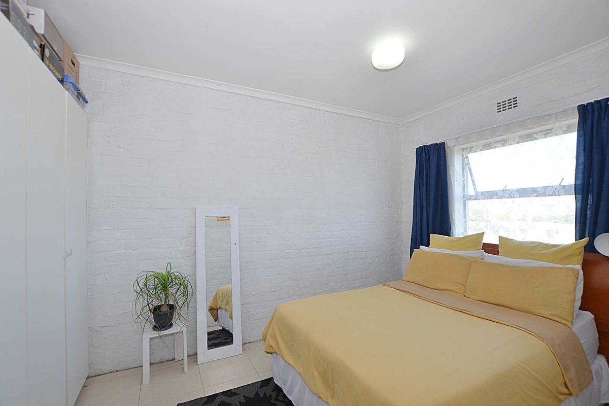 A bedroom featuring painted brick walls, tiled flooring, and a built-in wardrobe, offering a functional space with natural light from the awning window.