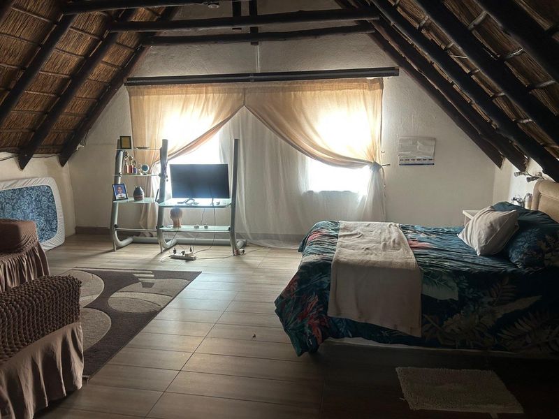 Spacious bedroom featuring a high vaulted thatch ceiling with exposed timber beams and tiled flooring, creating a rustic and airy atmosphere.
