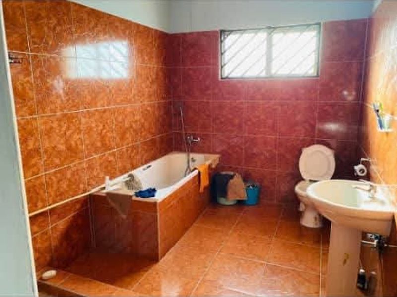 A dated bathroom featuring full-height orange ceramic wall tiles, a built-in bathtub, a pedestal sink, and a standard toilet.