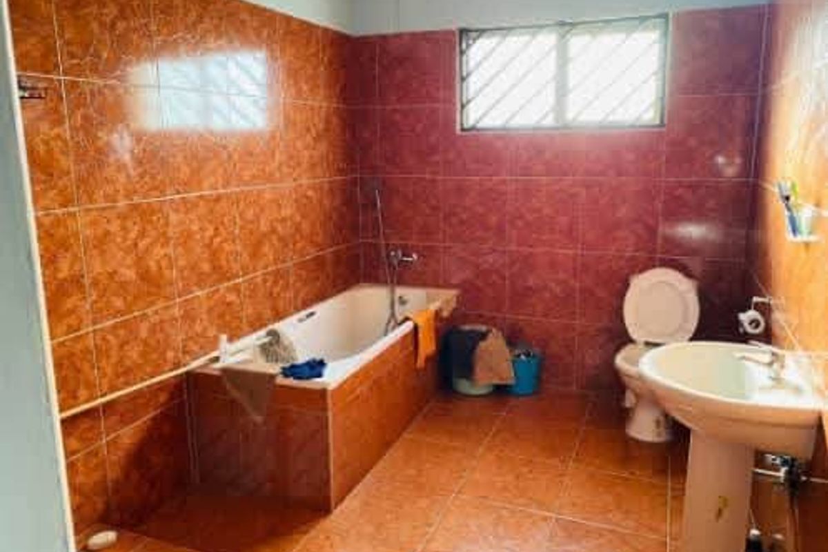 A dated bathroom featuring full-height orange ceramic wall tiles, a built-in bathtub, a pedestal sink, and a standard toilet.