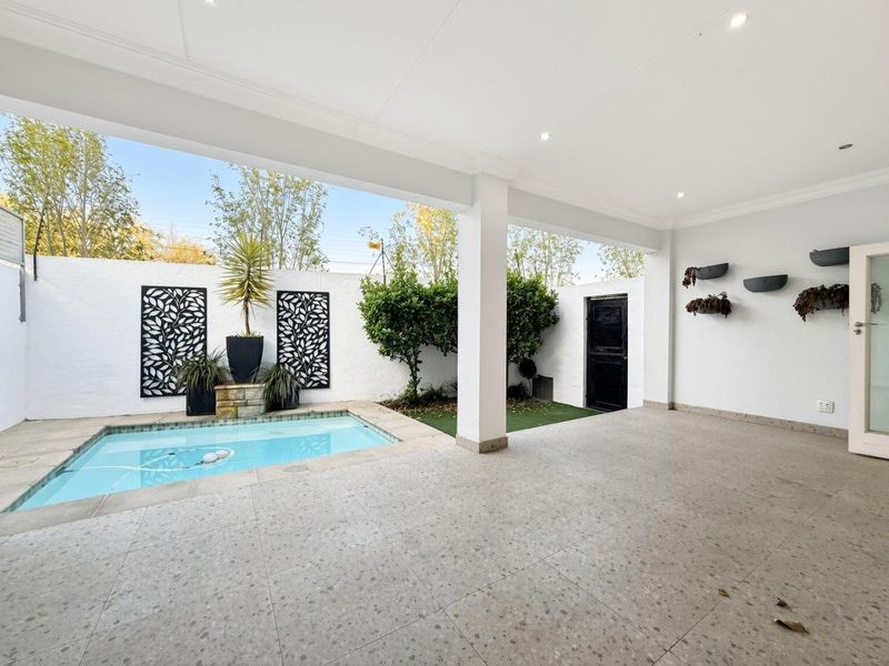 A clean, covered patio area featuring a built-in swimming pool, recessed lighting, and a low-maintenance tiled outdoor space.