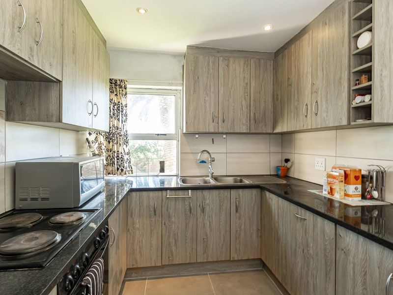 A functional kitchen featuring wood-look cabinetry, black granite countertops, a double basin sink, and integrated electric cooking appliances.