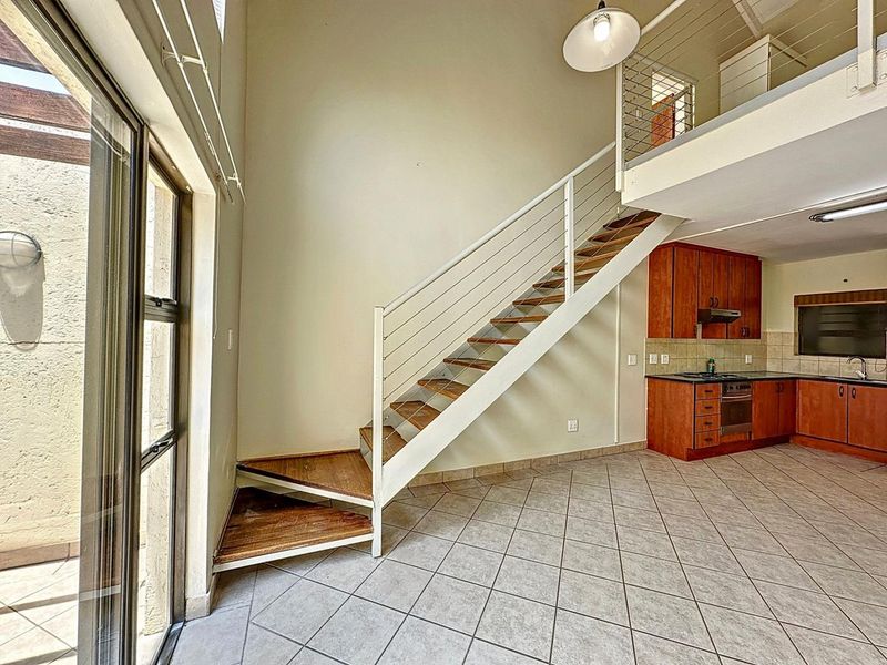 Open-plan living area featuring a mezzanine level, staircase, and a functional kitchen with built-in cabinetry and appliances, leading to an outdoor patio area.