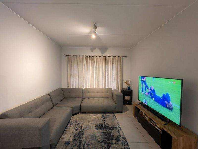A well-maintained living room featuring neutral tiled flooring and a window with a fitted curtain rod.