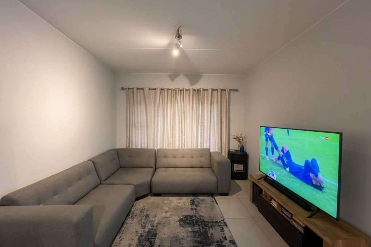 A well-maintained living room featuring neutral tiled flooring and a window with a fitted curtain rod.