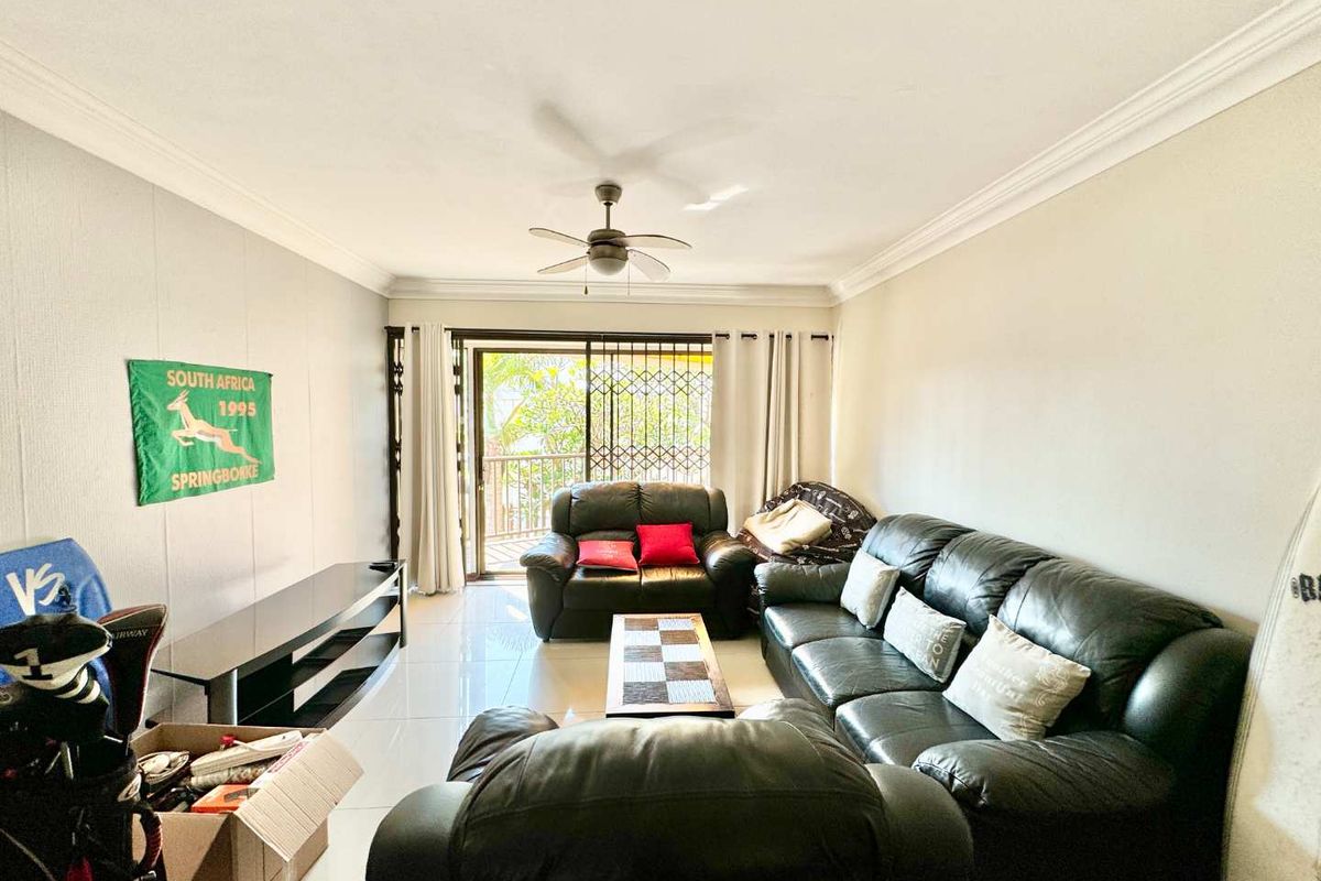 A spacious living room featuring tiled flooring, a ceiling fan, and sliding glass doors that open onto a balcony.
