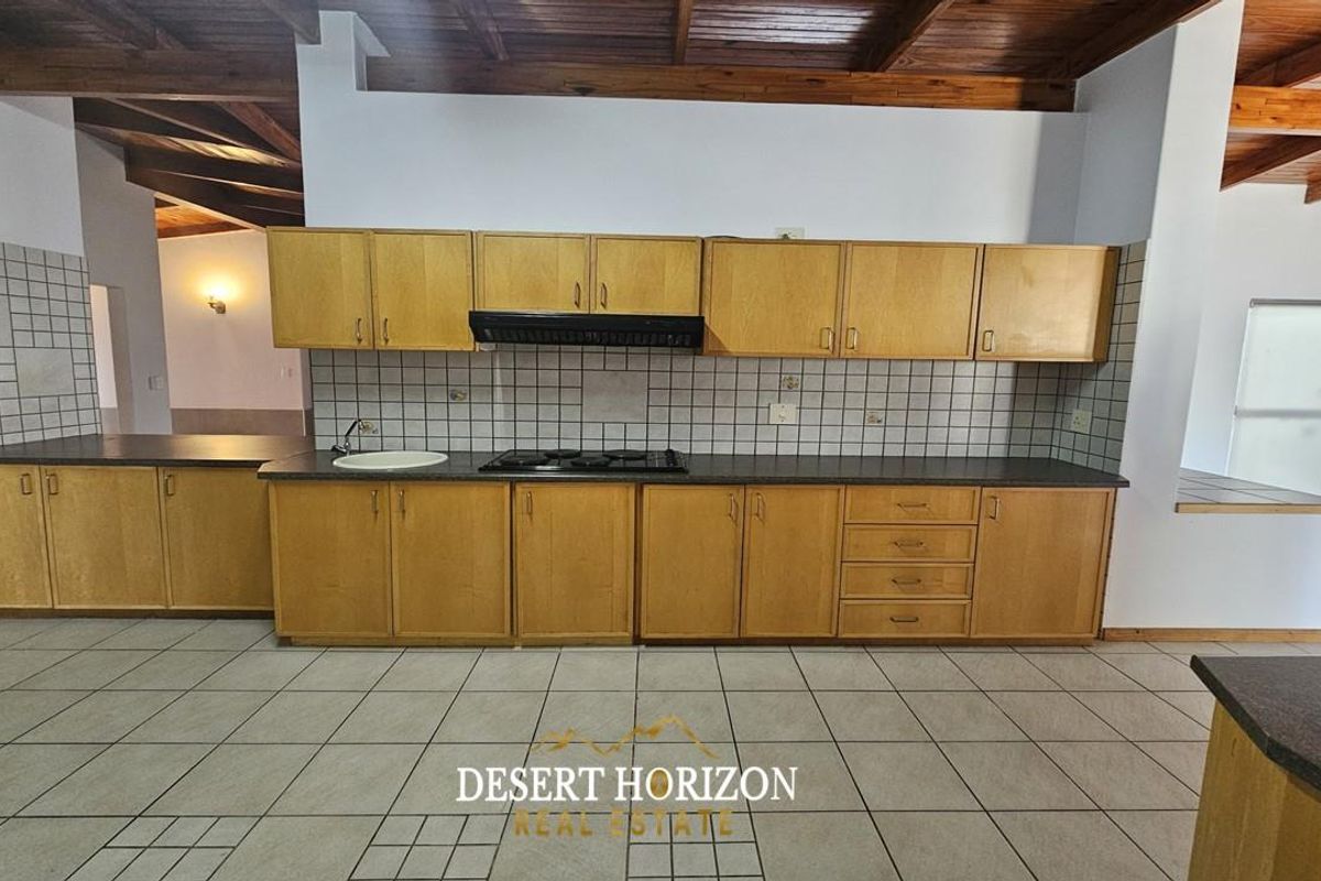 A functional kitchen featuring wooden cabinetry, a built-in hob, extractor fan, and tiled flooring under a vaulted timber ceiling.