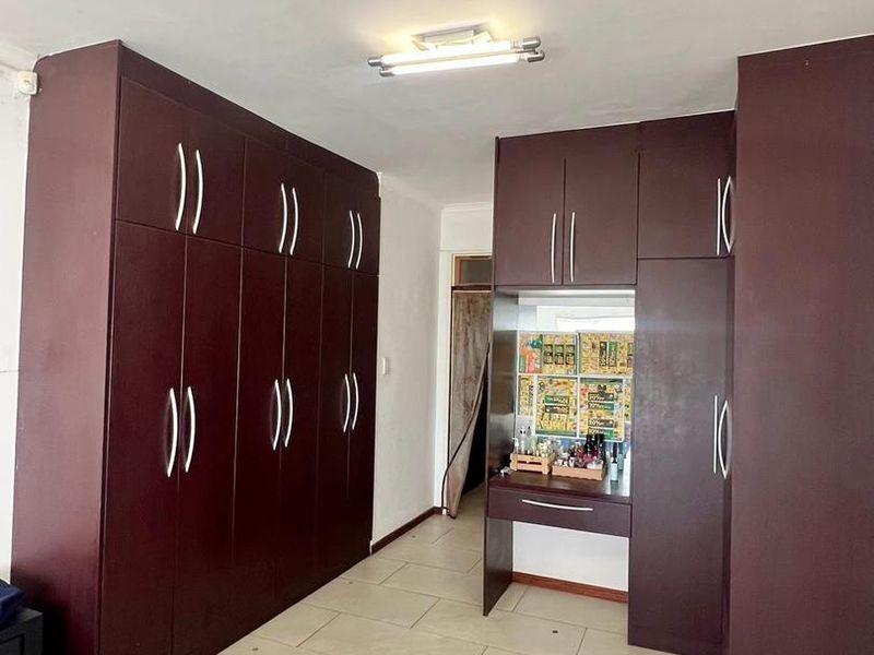 Bedroom featuring extensive dark wood built-in cupboards with an integrated vanity unit and neutral tiled flooring.