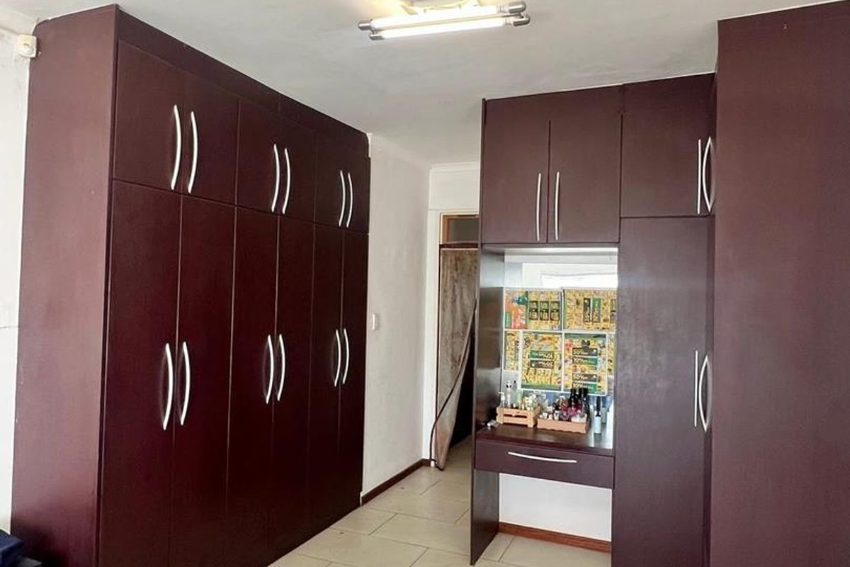 Bedroom featuring extensive dark wood built-in cupboards with an integrated vanity unit and neutral tiled flooring.