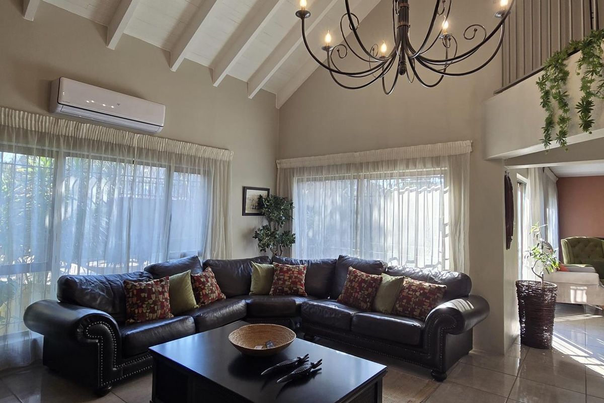 Spacious living room featuring a high vaulted ceiling with exposed rafters, tiled flooring, and a split-system air conditioner, overlooking a dining area.