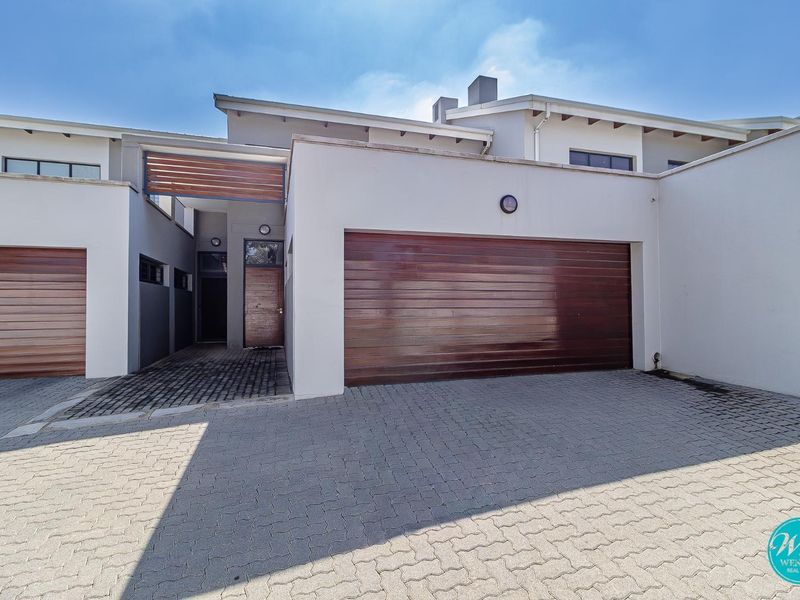 Modern townhouse exterior featuring a paved driveway, double garage with timber doors, and a covered entrance with timber detailing.