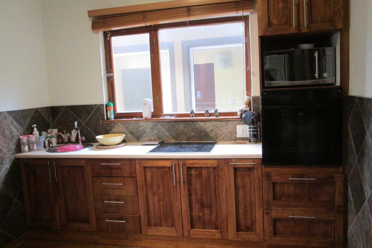 A functional kitchen featuring dark wood cabinetry, a built-in oven, microwave, hob, and tiled backsplash with a window overlooking the exterior.