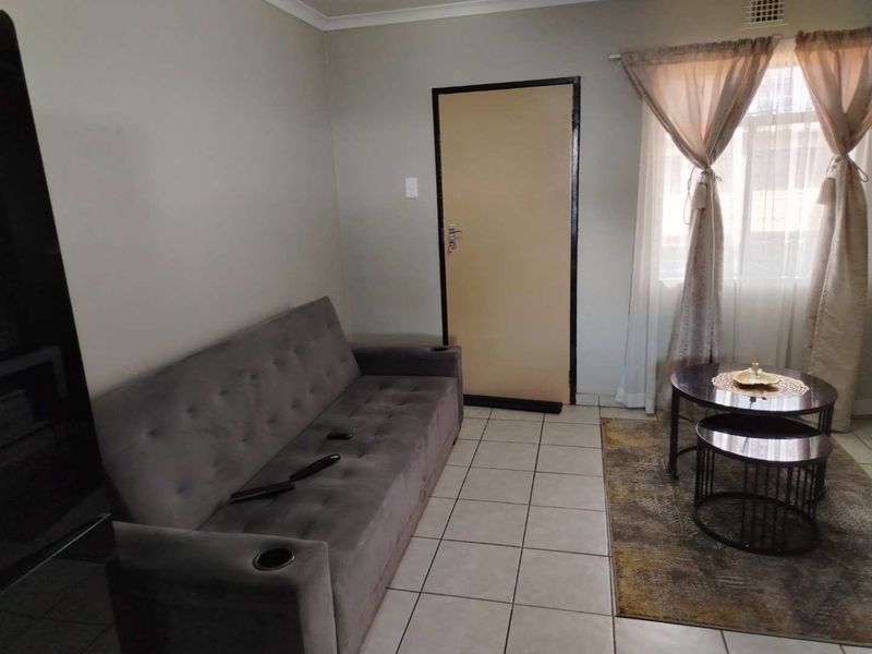 A functional living room featuring neutral wall tones, tiled flooring, and a standard internal door, providing a clean and simple base for interior design.