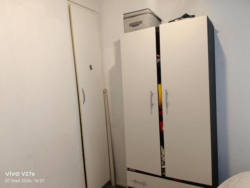 A bedroom corner featuring a built-in cupboard and a freestanding wardrobe with visible wear and misaligned door components.