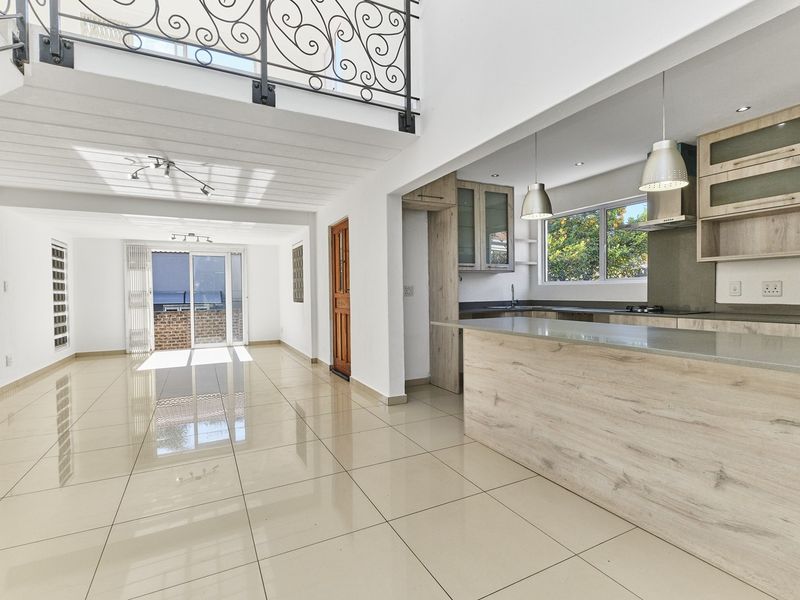 Spacious open-plan living and kitchen area featuring modern laminate cabinetry, stone countertops, polished tile flooring, and a striking wrought iron staircase railing.