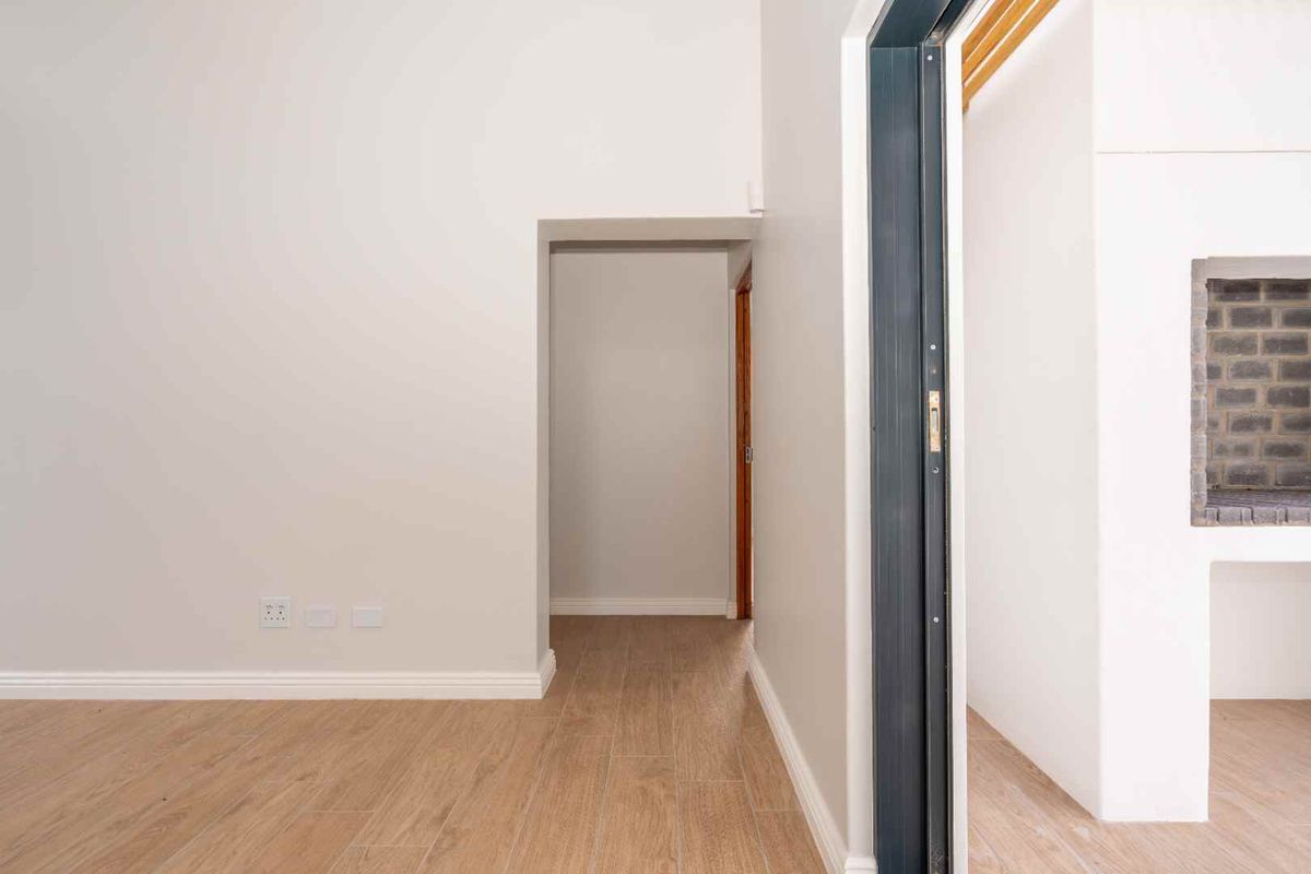 A bright interior space featuring wood-look tile flooring, neutral walls, and a built-in brick fireplace visible through the doorway.