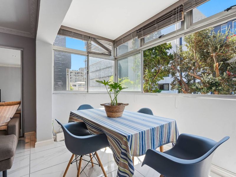 A bright, enclosed balcony or sunroom featuring large glass windows, tiled flooring, and recessed lighting, offering a pleasant space for dining or relaxation.