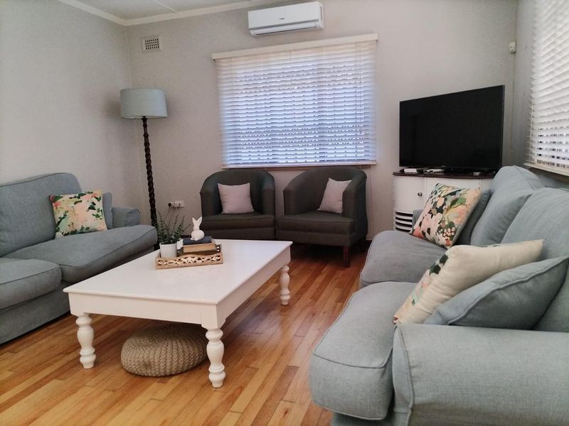 A comfortable living room featuring polished hardwood flooring, a wall-mounted split-system air conditioner, and venetian blinds for natural light control.