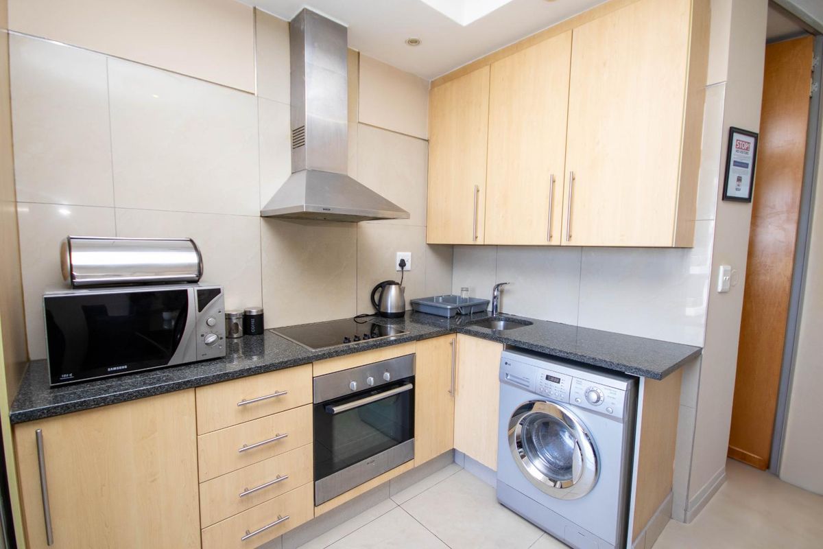 Compact kitchen featuring light wood cabinetry, granite countertops, integrated oven and hob, stainless steel extractor fan, and tiled finishes.