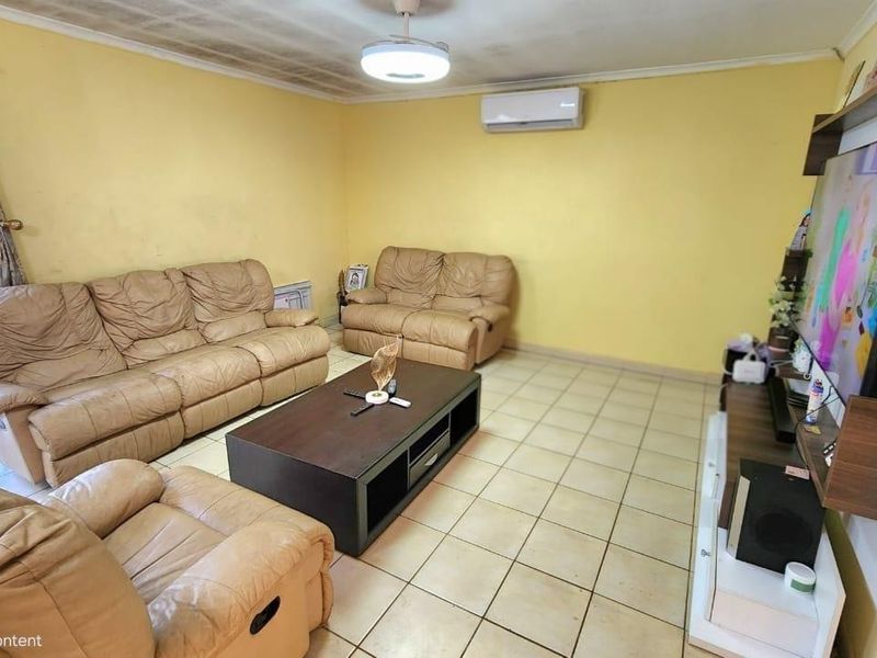 A living room featuring tiled flooring, a ceiling fan, and a wall-mounted air conditioning unit, showing signs of wear on the ceiling and walls.