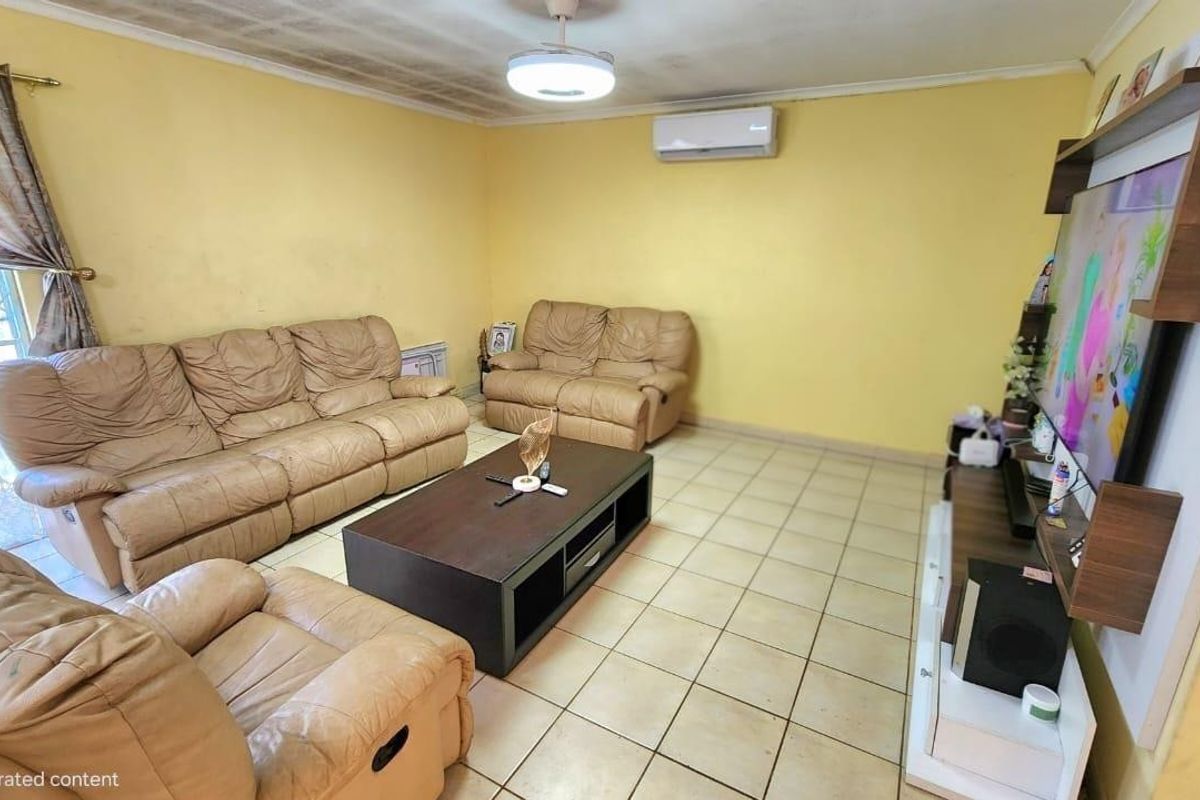 A living room featuring tiled flooring, a ceiling fan, and a wall-mounted air conditioning unit, showing signs of wear on the ceiling and walls.