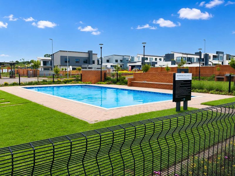 A well-maintained communal swimming pool area featuring paved surrounds, brick boundary walls, and secure mesh fencing within a residential estate.