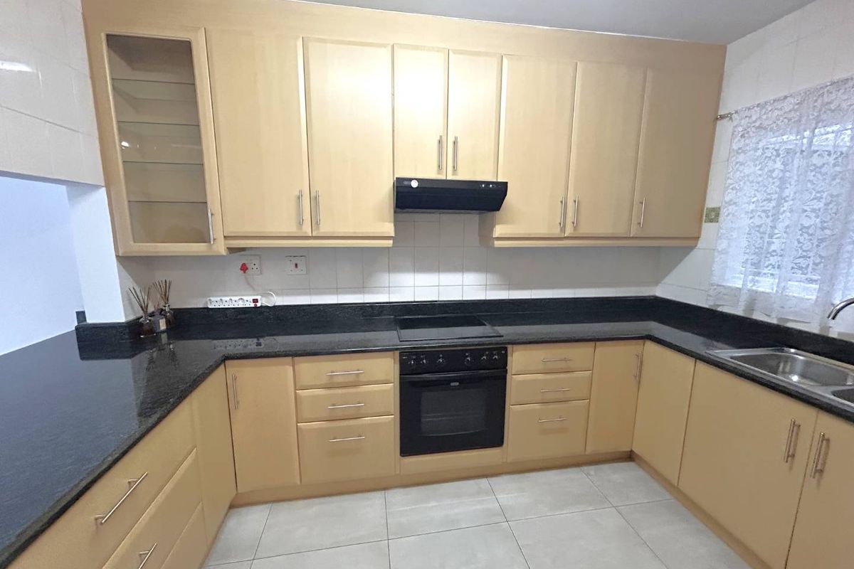 A functional kitchen featuring light wood-toned cabinetry, dark granite countertops, integrated oven and hob, and tiled flooring.