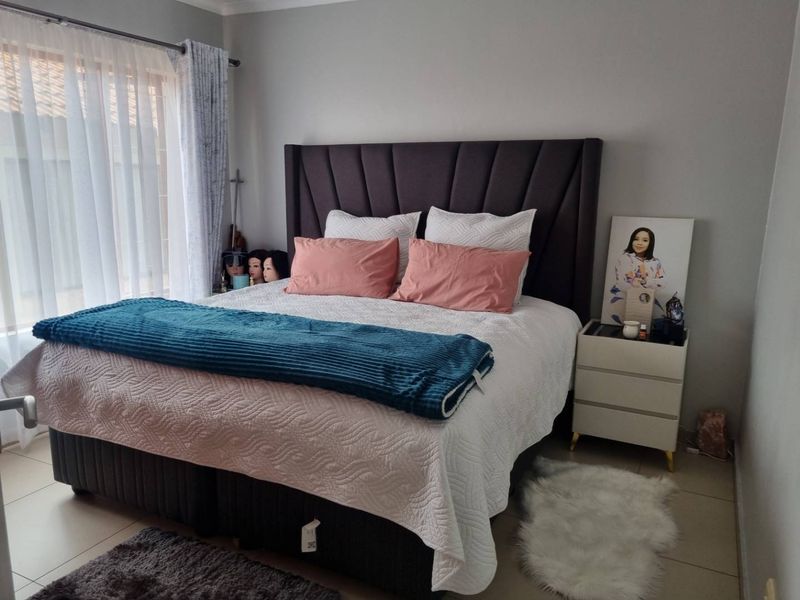 A well-maintained bedroom featuring neutral wall tones, tiled flooring, and large windows with curtain rails.