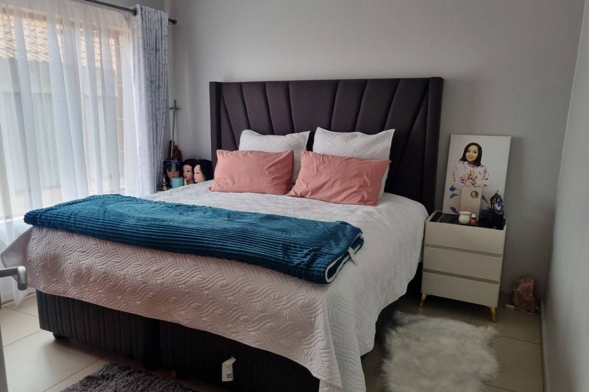 A well-maintained bedroom featuring neutral wall tones, tiled flooring, and large windows with curtain rails.