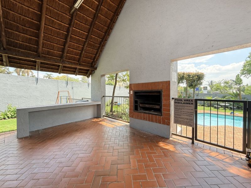 Covered outdoor entertainment area featuring a built-in brick braai, thatched roof, and direct access to the swimming pool.