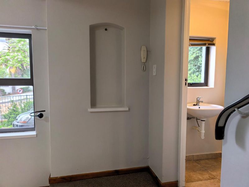 A functional hallway area featuring a recessed wall niche, intercom system, and direct access to a small bathroom with a wall-mounted basin.