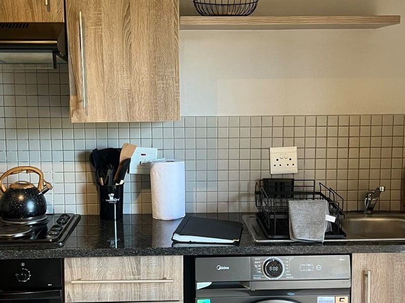 Modern kitchen featuring wood-grain cabinetry, granite-look countertops, tiled backsplash, built-in oven, gas hob, and an integrated washing machine.