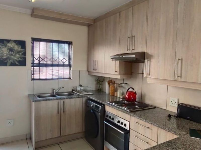 A functional kitchen featuring light wood-finish cabinetry, granite countertops, a built-in oven with hob, and an extractor fan, with direct access to a balcony.