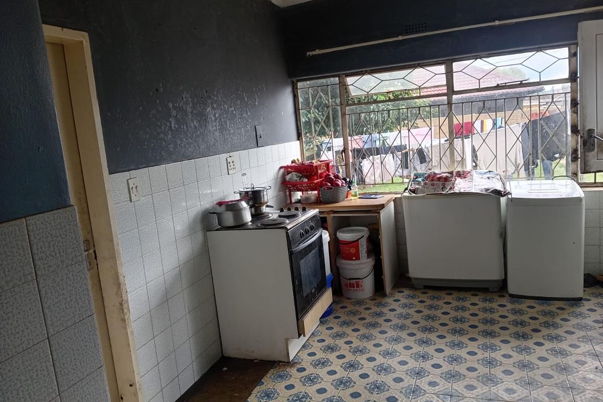 A functional kitchen area featuring tiled flooring, wall-mounted splashback tiles, and a built-in stove, with large windows providing natural light and garden views.