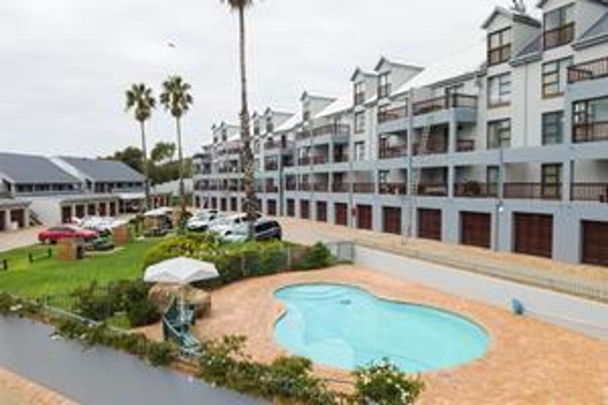 An elevated view of the apartment complex featuring a communal swimming pool, landscaped garden area, and ground-level garage access.