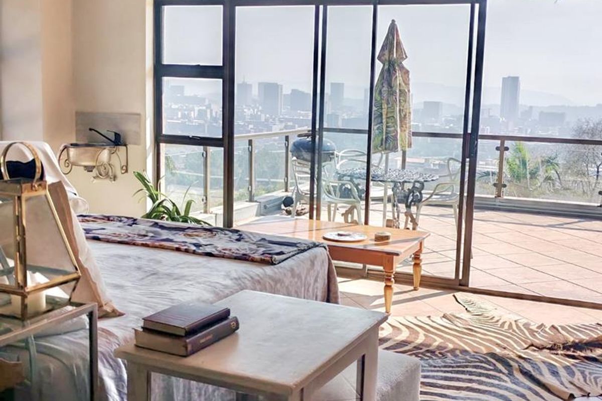 Spacious bedroom featuring exposed timber ceiling beams, tiled flooring, and large sliding glass doors opening onto a balcony with expansive city views.