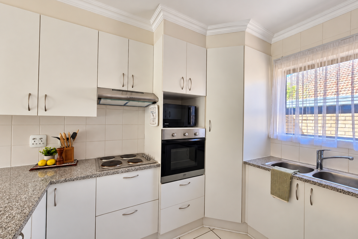 A well-maintained kitchen featuring white cabinetry, granite countertops, built-in oven, electric hob, and a double stainless steel sink with tiled splashbacks.