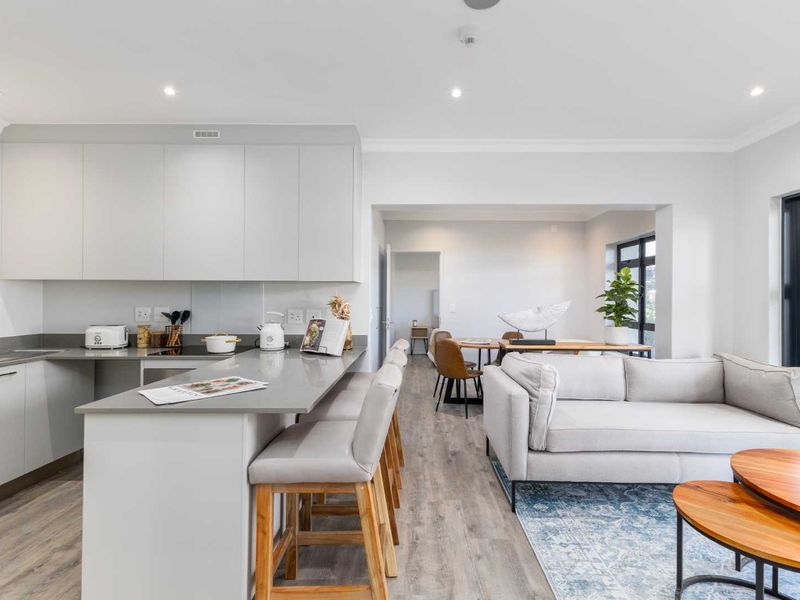 Modern open-plan kitchen and living area featuring sleek cabinetry, quartz countertops, laminate flooring, and large windows providing ample natural light.