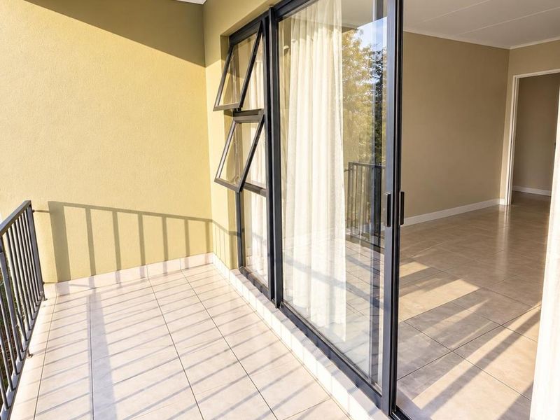 A clean, tiled balcony featuring a metal balustrade and large sliding glass doors providing access to the interior living space.